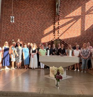 Eine große Gruppe Menschen steht im sonnigen Vorraum einer Kirche
